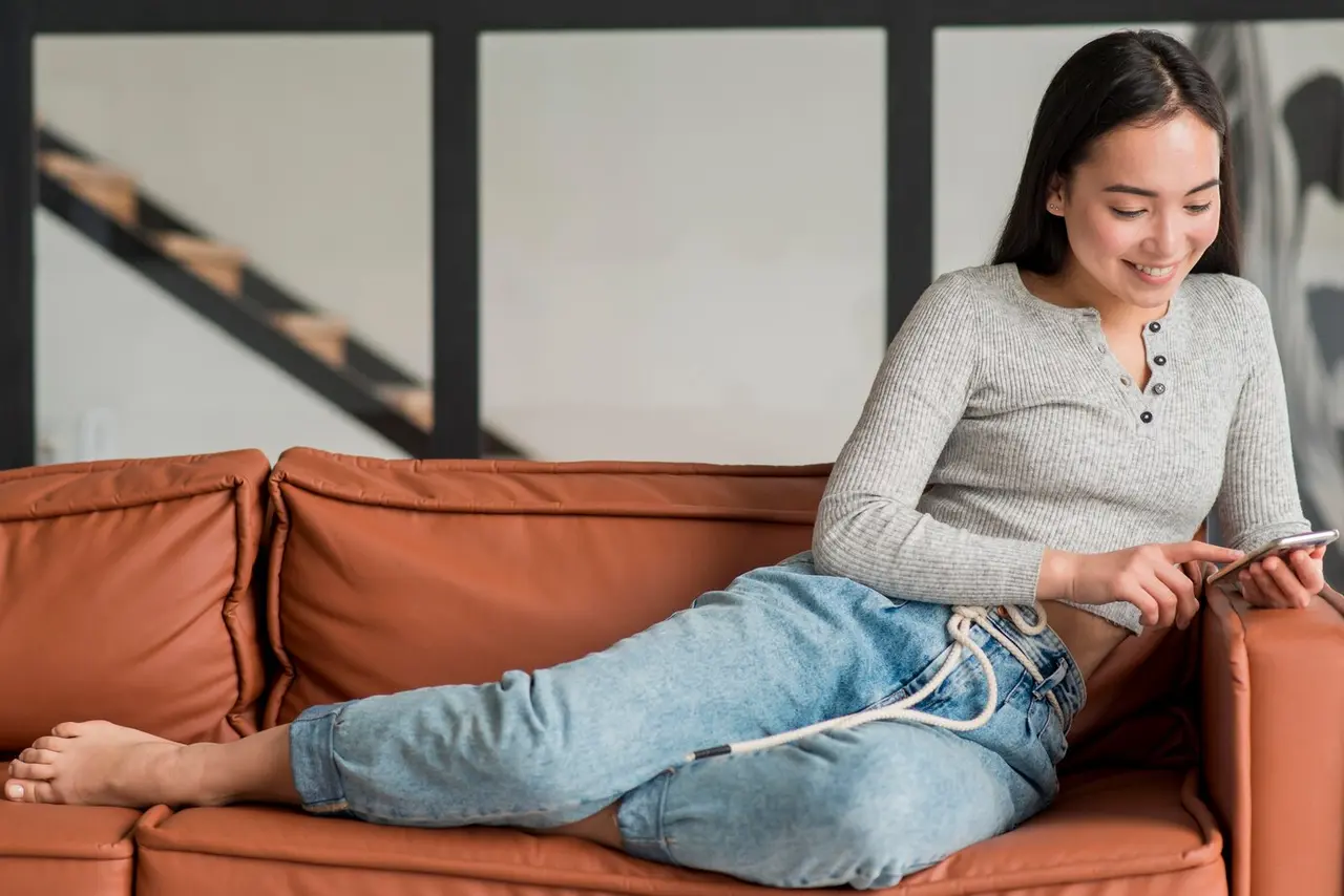 Girl happily playing with phone sitting on sofa