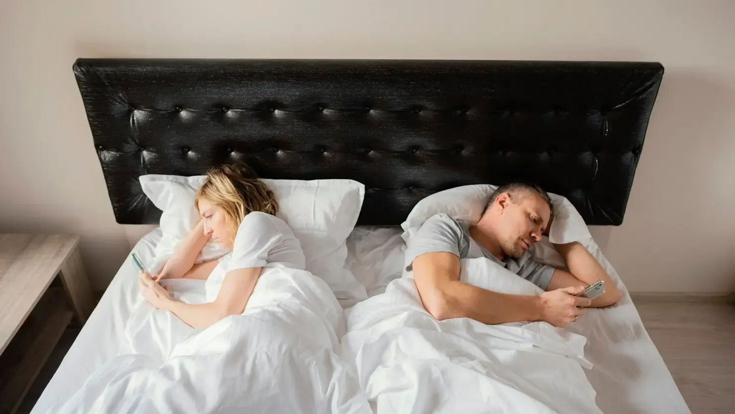 Couple lying back to back playing with phones