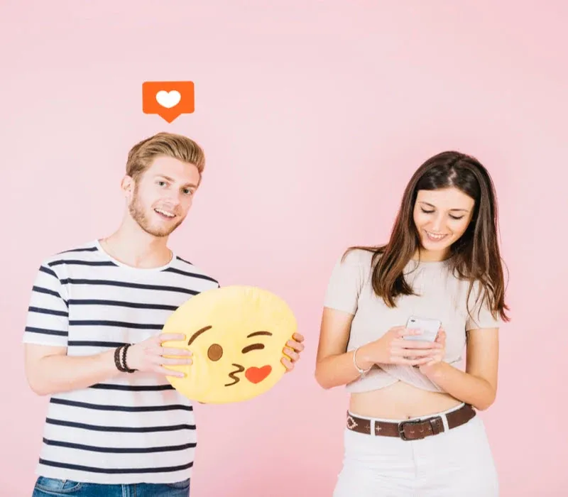 A man is holding kiss emoji near his girlfriend using smartphone.