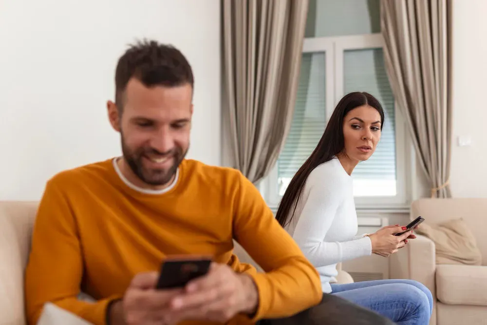 Woman wondering who her smiling husband is texting